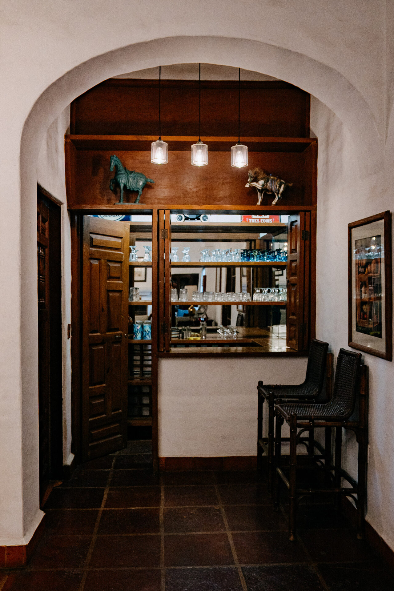 Cantina de Quinta La Joya con barra de madera, cristalería y bancos, vista bajo el arco de la casa principal