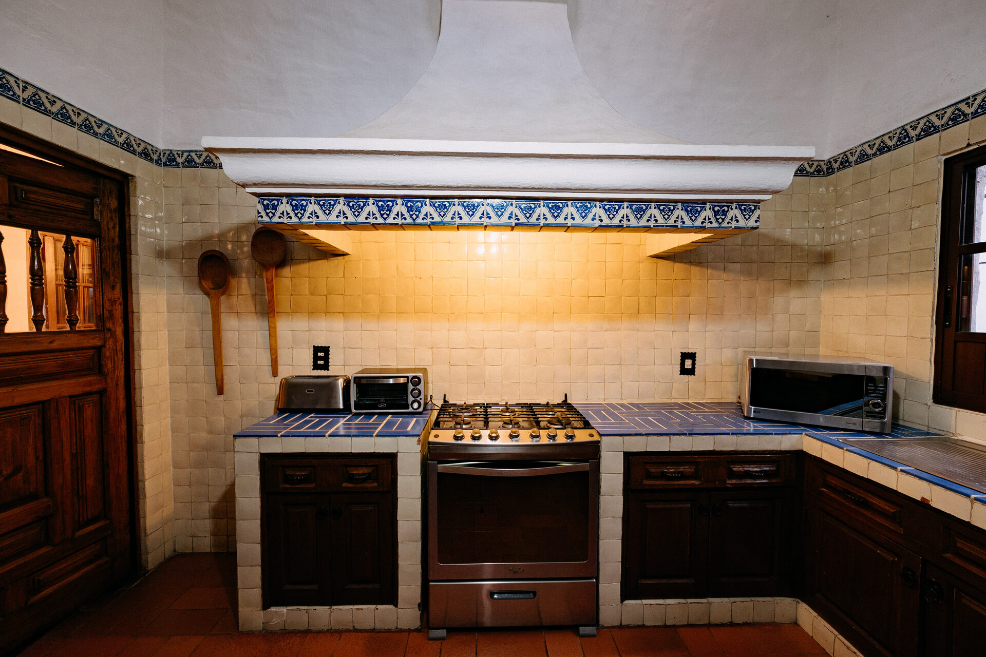 Cocina de Quinta La Joya iluminada de noche, con campana de mampostería, cenefa de talavera, gabinetes de madera maciza y cubiertas de azulejo azul