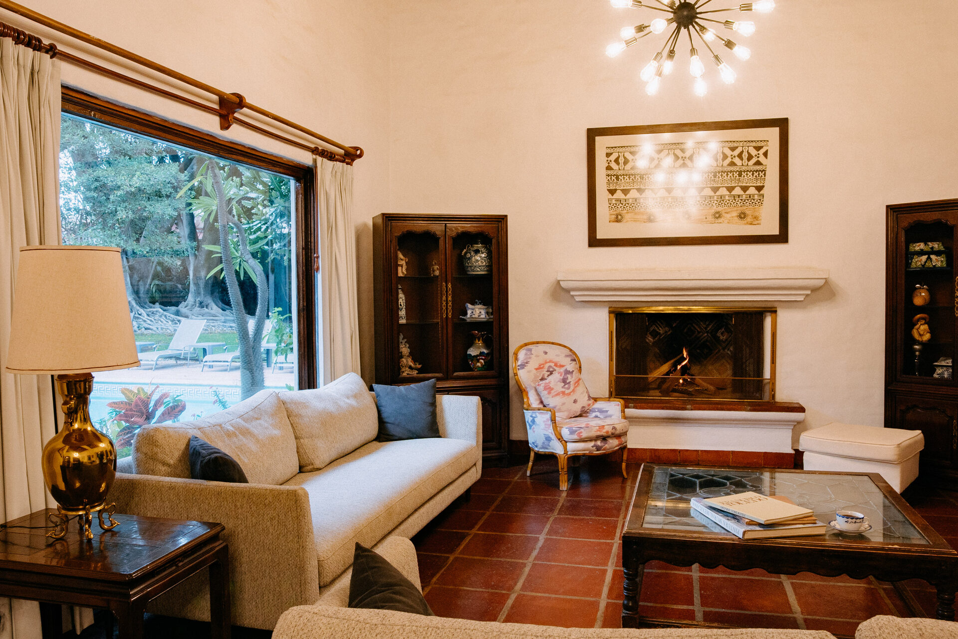 Sala de Quinta La Joya con chimenea encendida, ventanal al jardín y piso de barro