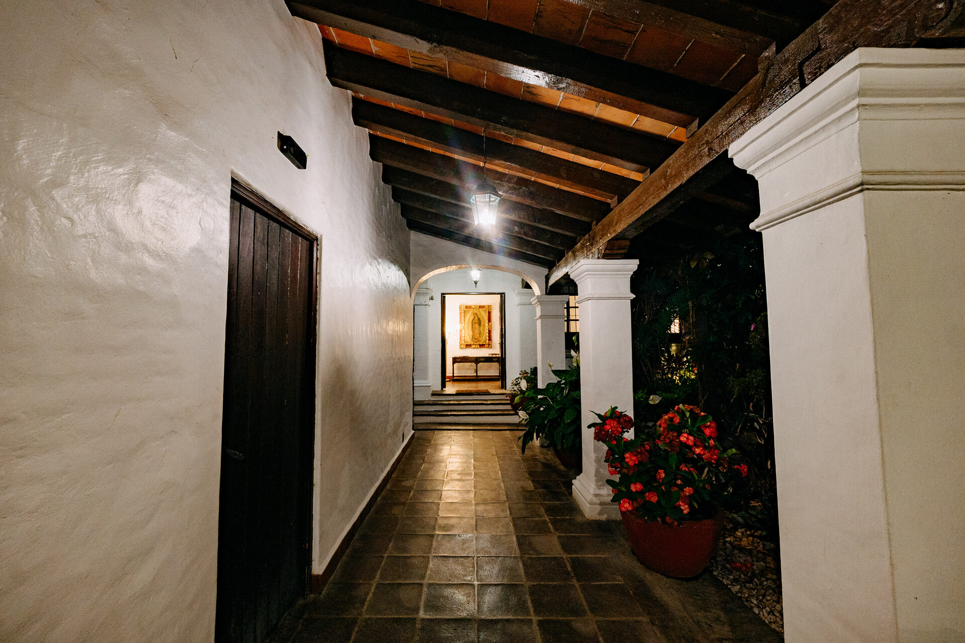 Corredor interior de Quinta La Joya con columnas de cantera, techo de viga de madera y una puerta iluminada al fondo