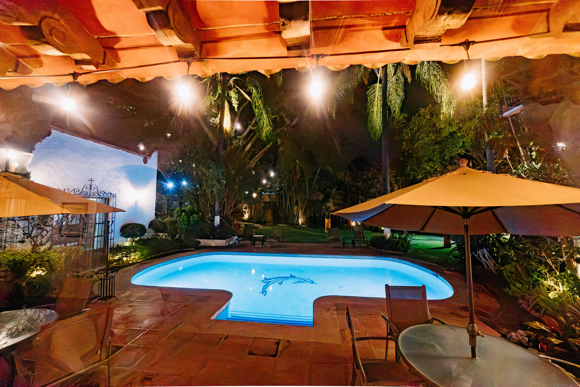 Terraza techada de Quinta La Joya al anochecer, con vigas de madera, faroles encendidos y la alberca iluminada al frente