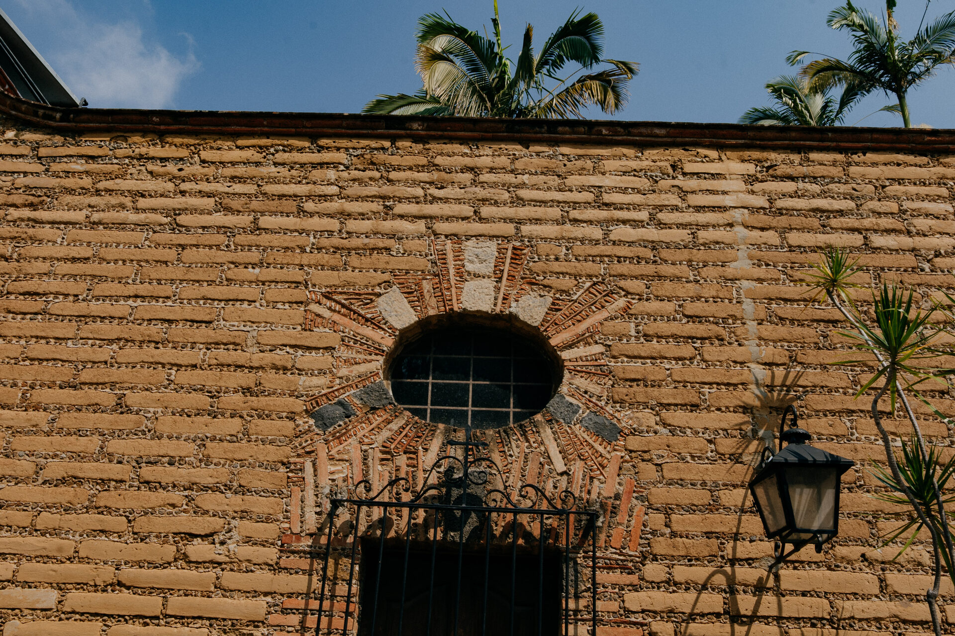 Portón de madera de Quinta La Joya enmarcado por un arco de ladrillo en forma de sol sobre muro de adobe