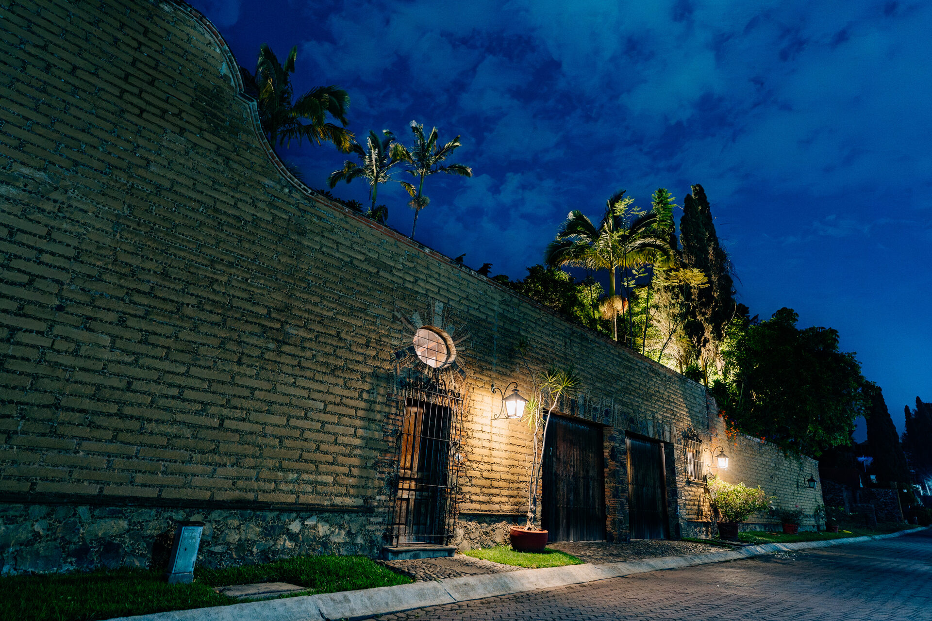 Muro de adobe de Quinta La Joya al anochecer, iluminado a lo largo de la calle empedrada en Cuernavaca