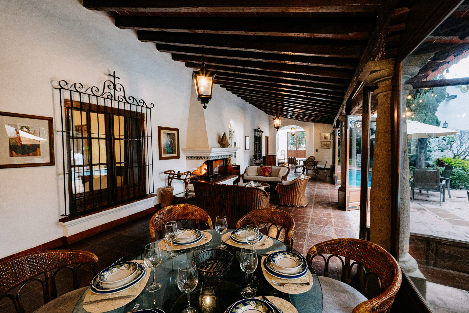 Vista diurna de la terraza de Quinta La Joya: arcada de columnas blancas, techo de viga, chimenea encendida y comedor hacia el jardín